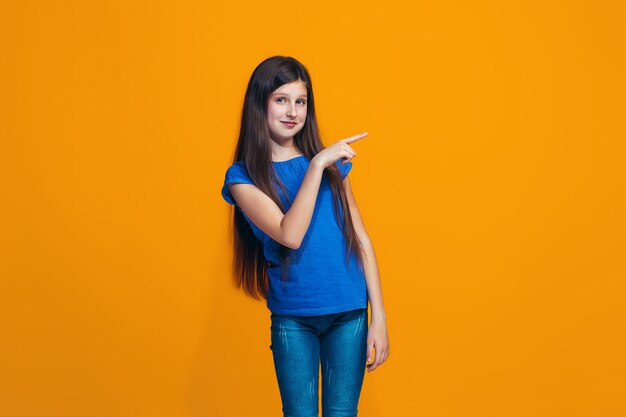 The happy teen girl standing and smiling against orange background.