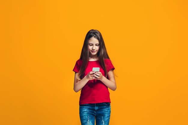 The happy teen girl standing and smiling against orange space.