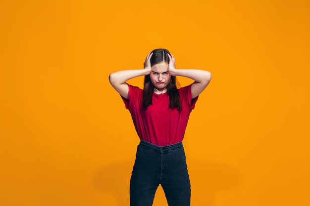 The happy teen girl standing and smiling against orange wall