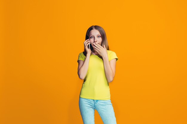 The happy teen girl standing and smiling against orange wall