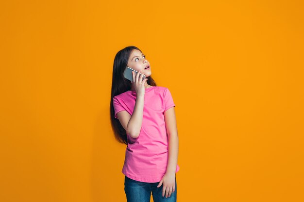 The happy teen girl standing and smiling against orange.