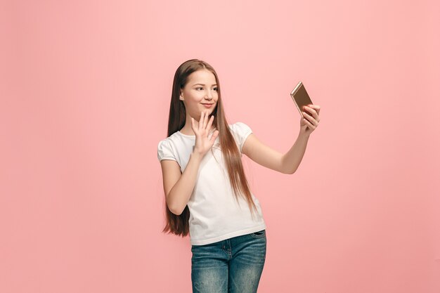立っている幸せな十代の少女、ピンクのスタジオの背景に笑みを浮かべて、