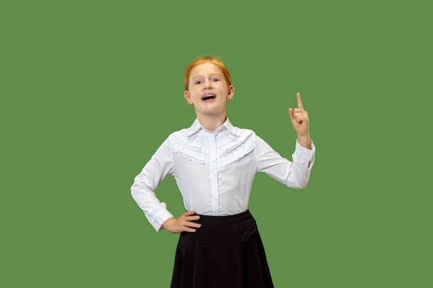 Happy teen girl standing, smiling and pointing up isolated on trendy green studio background. Beautiful female half-length portrait.