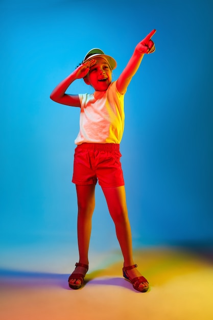 Счастливая девушка-подросток стоит, улыбается и указывает вверх над модной синей неоновой студией