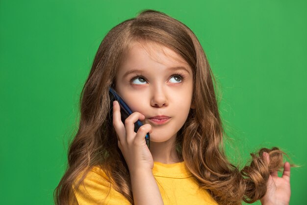 Happy teen girl standing, smiling with mobile phone over trendy green. Beautiful female half-length portrait