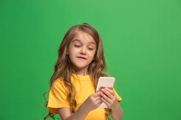 Счастливый подросток девушка стоя, улыбаясь с мобильным телефоном на фоне модных зеленых студии.