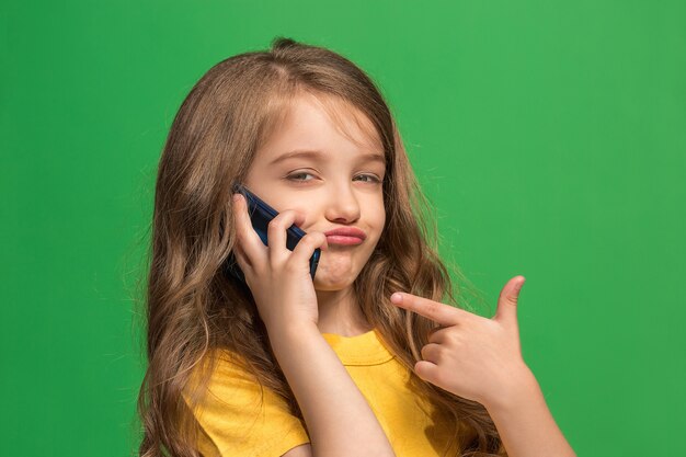 Happy teen girl standing, smiling with mobile phone over trendy green studio background.