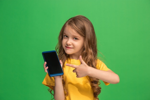 Free photo happy teen girl standing, smiling with mobile phone over trendy green studio wall