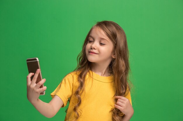 トレンディな緑のスタジオの壁を越えて携帯電話で笑って立っている幸せな十代の少女