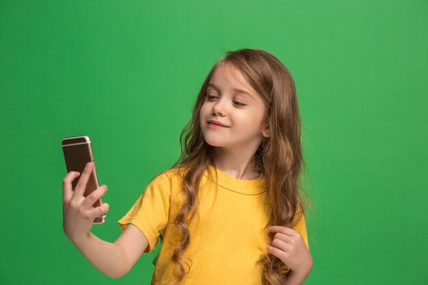 Happy teen girl standing, smiling with mobile phone over trendy green studio wall