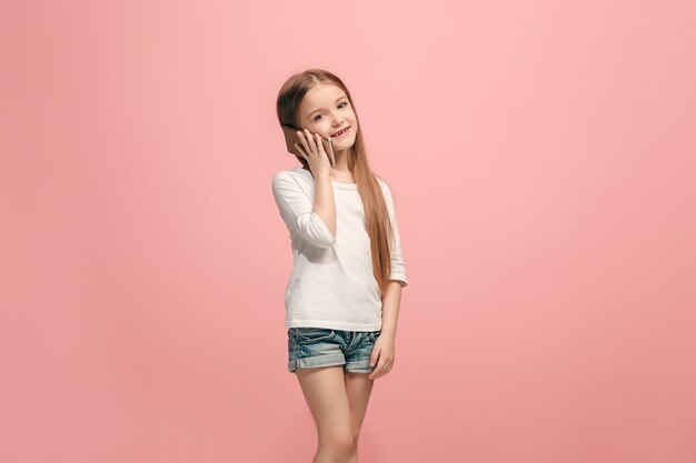 Happy teen girl standing, smiling with mobile phone over trendy pink studio background. Beautiful female half-length portrait