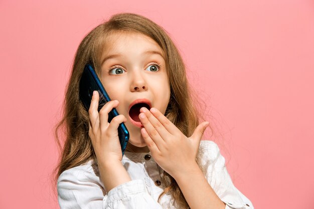 Happy teen girl standing, smiling with mobile phone over trendy pink studio