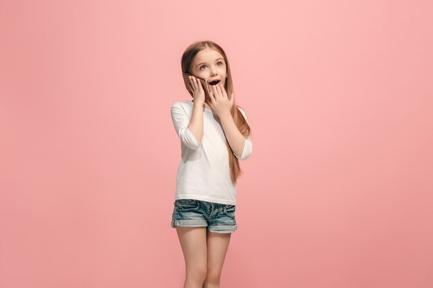 Happy teen girl standing, smiling with mobile phone over trendy pink  wall. Beautiful female half-length portrait. Human emotions, facial expression concept.