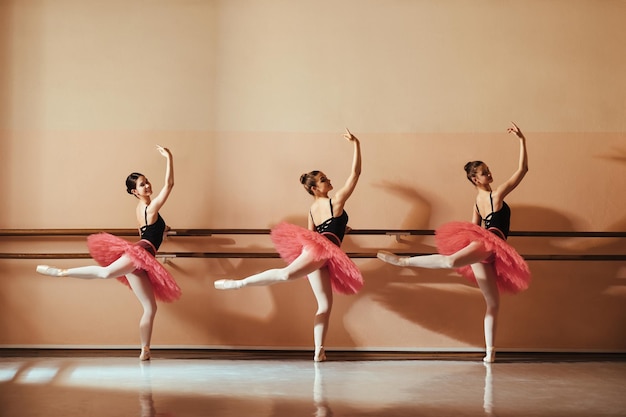 Happy teenage ballet dancers holding on a barre while dancing at ballet school Copy space