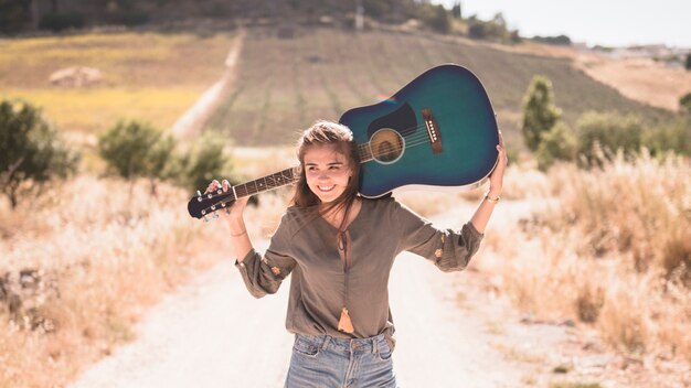 Счастливый девочка-подросток держит гитару на открытом воздухе