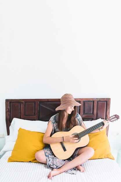 Happy teenage girl playing guitar in bedroom