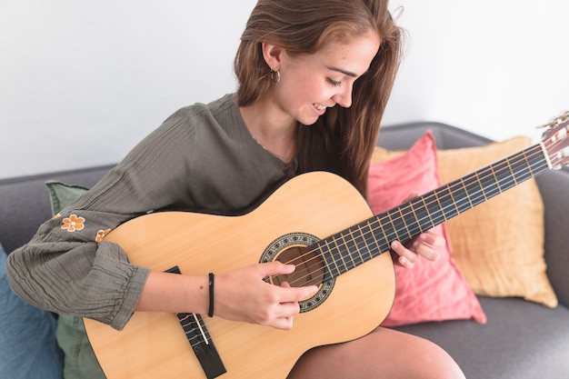 Happy teenage girl playing guitar at home