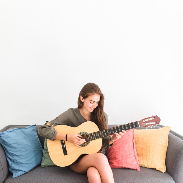 白い背景にギターを弾くソファに座っている幸せな十代の少女