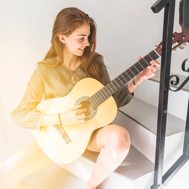 Free photo happy teenage girl sitting on staircase playing guitar