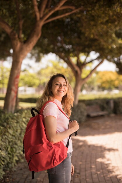 Счастливая девушка улыбается с рюкзаком в парке