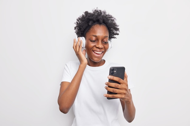Happy teenage girl with Afro hairstyle choose song from playlist holds mobile phone 