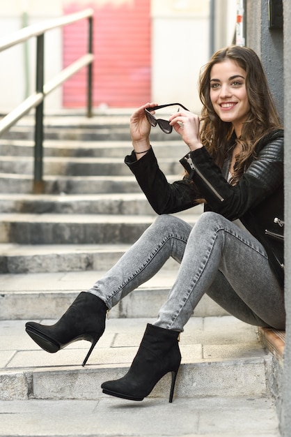 Foto gratuita adolescente felice che tiene i suoi occhiali da sole e si siede sulle scale