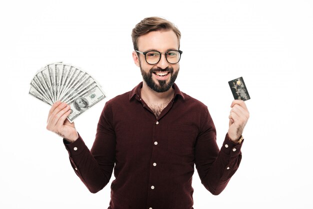 Счастливый думая молодой человек держа деньги и кредитную карточку.