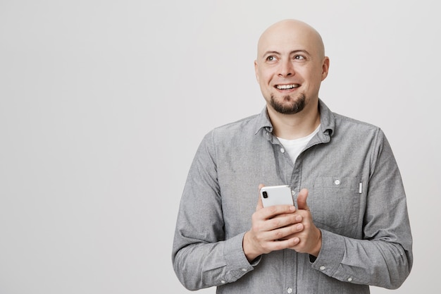 Happy thoughtful bald man look away, smiling as using mobile phone