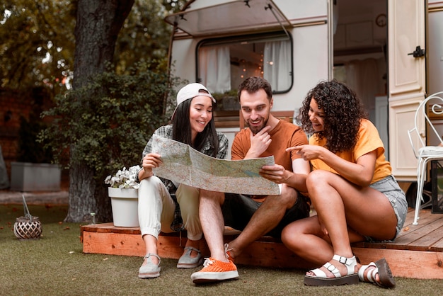 Free photo happy three friends looking on a map in front of van long shot