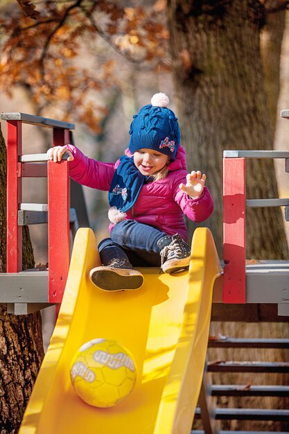 Happy three-year baby girl in jacket on slide