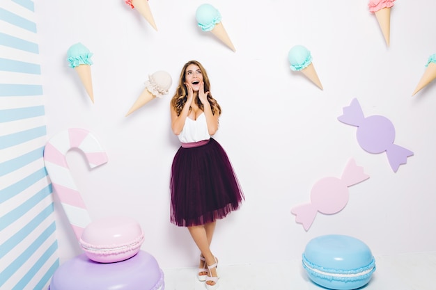 Happy time of joyful young woman in tulle skirt isolated among sweets. Pastel colors, macarons, ice cream, happiness, fashionable model, having fun.