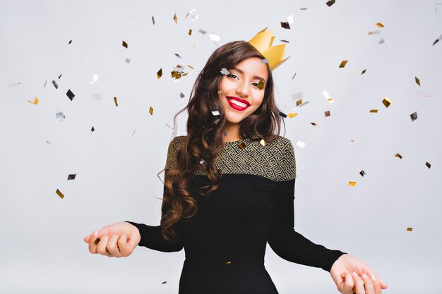 Happy time, young smiling woman celebrating new year, wearing black dress and yellow crown, happy carnival disco party, sparkling confetti, having fun, smiling.