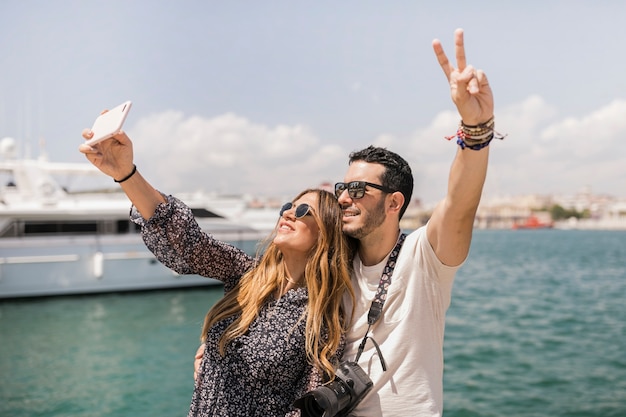 Happy tourist couple taking selfie on cell phone against the sea