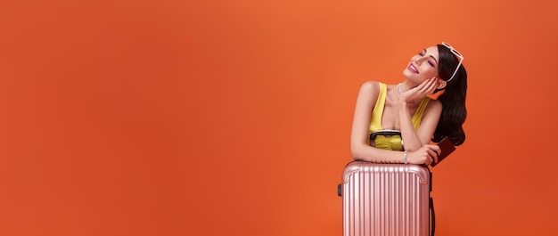Happy tourist woman girl with suitcase and passport on copy space orange background