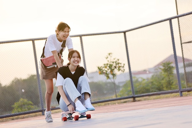 Счастливые две азиатские девушки-подружки-подростки со скейтбордом на солнце, играющие вместе в летний день и скейтбординг