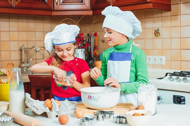 Счастливые двое веселых детишек готовят тесто, пекут печенье на кухне