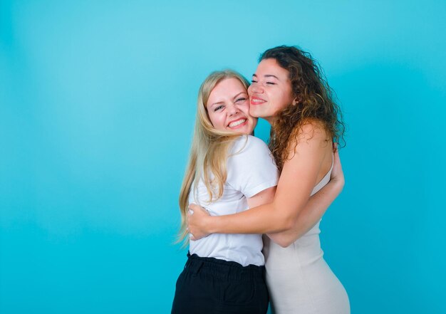 Happy two girls are hugging each other on blue background