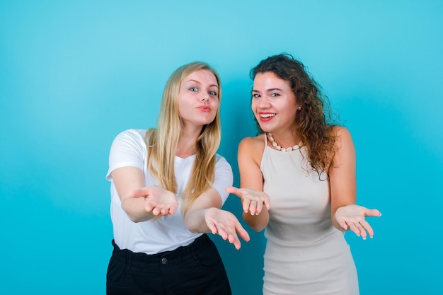 Free photo happy two girls are opening and showing their hadfuls on blue background