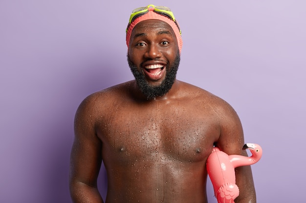 Free photo happy unshaven muscular guy has good mood after swimming and diving in sea, smiles broadly, carries inflated swimring