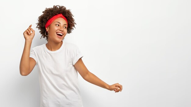 Happy upbeat woman raises arms, looks away with delighted expression, dressed in casual wear