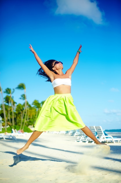 счастливая городская современная молодая стильная женщина женщина модель в яркой современной ткани в зеленой красочной юбке на открытом воздухе летом пляж прыгает за голубым небом