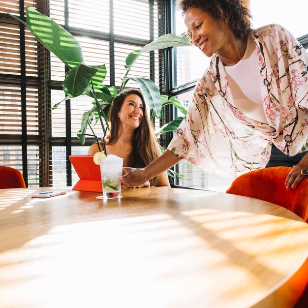 Happy waitress serving cocktail to female customer sitting in the restaurant