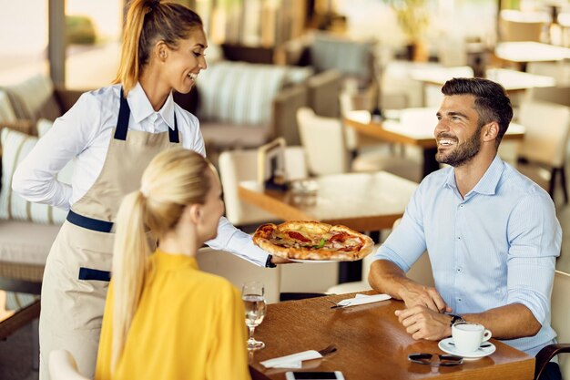 レストランでカップルにピザを提供する幸せなウェイトレス