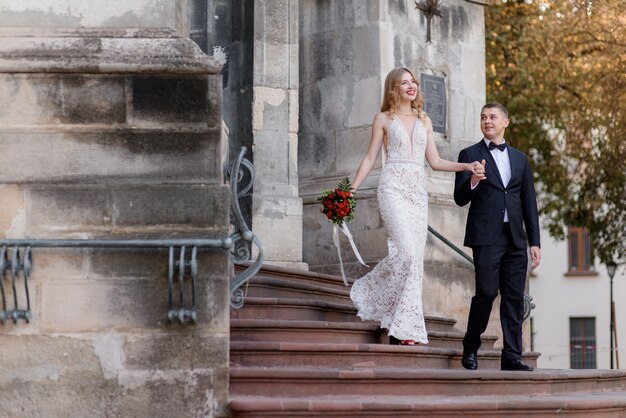 幸せな結婚式のカップルが階段の上の教会から出てくる一緒に手を繋いでいます。