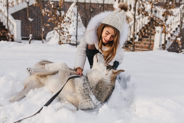 Happy winter time of joyful young woman playing with cute husky dog in snow on street. Cheerful mood, positive emotions, real friendship with pets, love animals