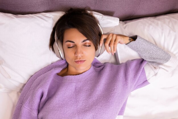 Бесплатное фото Счастливая женщина дома на удобной кровати в теплом свитере, слушает музыку
