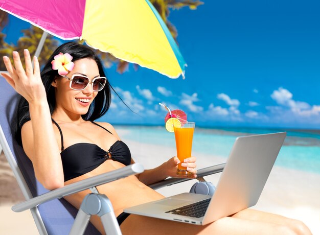 Счастливая женщина на пляже с портативным компьютером.