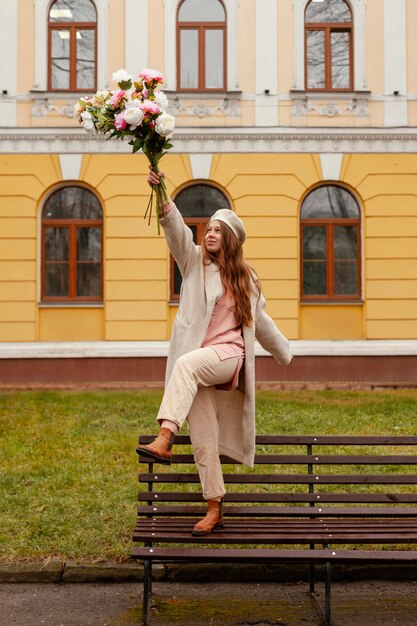 Happy woman on the bench outdoors holding bouquet of flowers in the spring