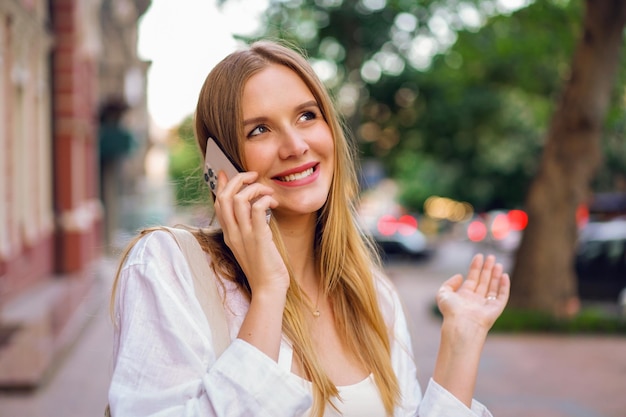행복 한 여자 전화입니다. 그녀의 스마트폰으로 말하는 예쁜 금발 여성의 라이프스타일 야외 초상화.