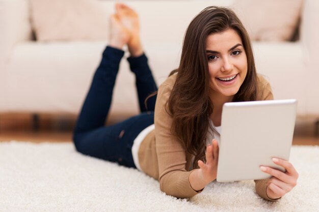 Счастливая женщина на ковре с помощью цифрового планшета